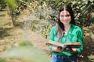 Smiling serene young woman reading a book in the greenery of the field. Benefits of reading