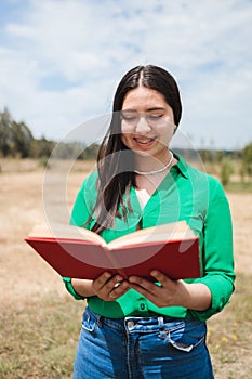 Smiling serene young woman reading a book in the greenery of the field. Benefits of reading