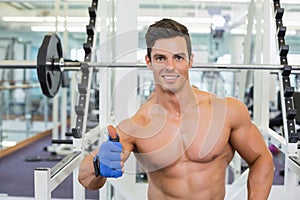Smiling shirtless muscular man giving thumbs up in gym