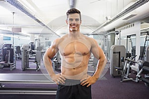 Smiling shirtless muscular man with hands on hips in gym