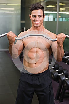 Smiling shirtless muscular man lifting barbell in gym