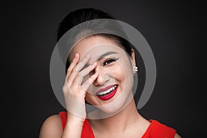 Smiling shy woman closed her face with a hand over black background.