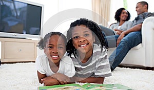 Smiling siblings reading lying on the floor