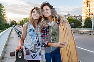 Smiling skateboarding girls standing in the street hanging out, holding longboards