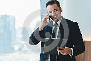 Smiling skilled businessman talking phone while looking at data. Ornamented.