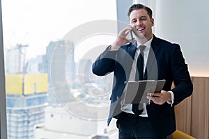 Smiling skilled businessman talking phone while looking at data. Ornamented.