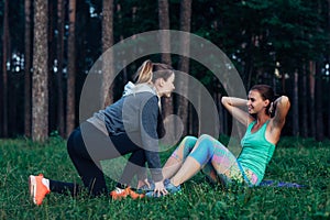 Smiling slim girl doing sit-ups while female friend assisting her holding down the feet. Two girlfriends training