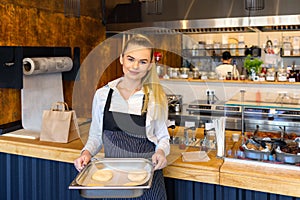 Smiling small business owner holding tray of bread dough, Happy baker with apron working in commercial kitchen