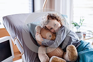 Smiling small girl with teddy bear in bed in hospital.