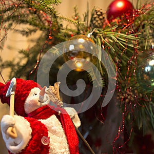 Smiling snowman in a red hat looks at the sparkling Christmas-tree decorations