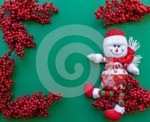 Snowman figurine on red sorb rowan branches green Christmas background