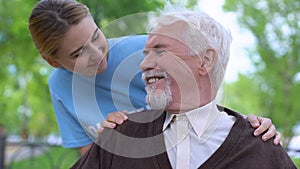 Smiling social worker taking care of aged pensioner, nursing home volunteering