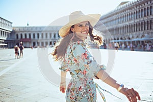 Smiling solo tourist woman in floral dress having walking tour photo