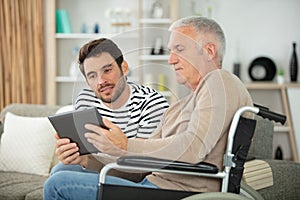 smiling son and father in wheelchair with tablet photo