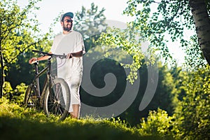 Smiling sport boy stand on a grass with bicycle outdoor