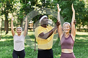 Smiling sports trainer assisting active senior woman in outdoor workout