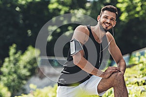 smiling sportsman in earphones with smartphone in running armband case doing