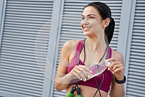 Smiling sporty brunette opening a water bottle