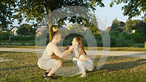 Smiling sporty couple holding hands while doing bodyweight squats at sunny park.