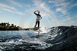 smiling sporty man in black wetsuit riding the wave on hydrofoil board