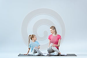 Smiling sporty mother and daughter practicing gomukhasana yoga pose