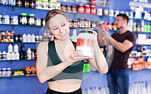 Smiling sporty woman holding jar of sports supplements products