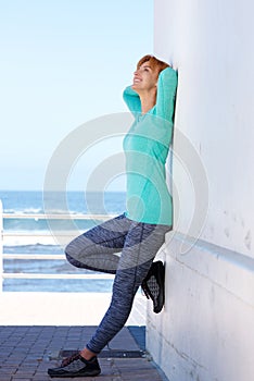 Smiling sporty woman standing by sea leaning on wall