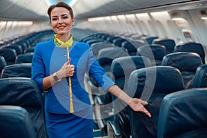 Smiling stewardess pointing at passenger seat in airplane cabin