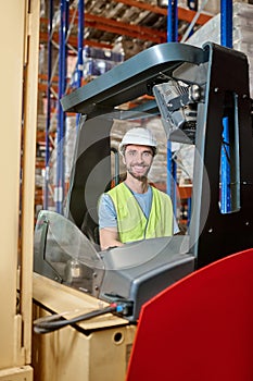 Smiling storehouse employee seated in the forklift