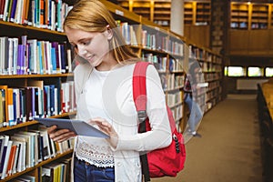 Smiling student with backpack using tablet in library