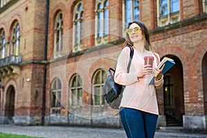 Smiling student with bag and take away coffee in campus garden