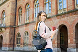 Smiling student with bag and take away coffee in campus garden