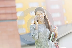 Smiling student with books talking on smartphone at university campus