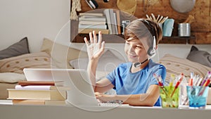 Smiling student boy studying at home with remote school connected to computer on the web, raise his hand to answer questions or