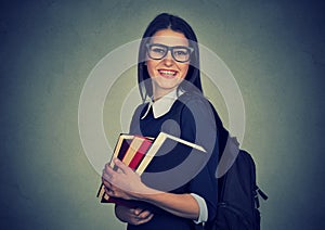 Smiling student carrying a backpack and holding stack of books