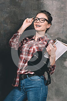 Smiling student with copybook standing at wall