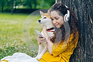 Smiling student enjoying music in headphones using smartphone in park with dog