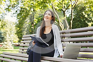 Smiling student girl sitting in park using laptop