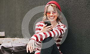 Smiling student girl using mobile phone while sitting outside   in morning