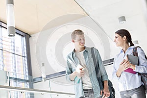 Smiling students with books talking while walking in corridor at university