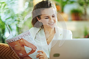 Smiling stylish female with laptop and magazine