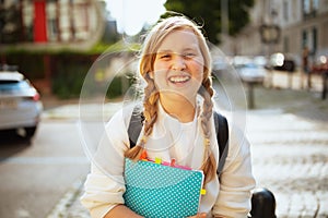 Smiling stylish pupil crossing crosswalk outdoors in city