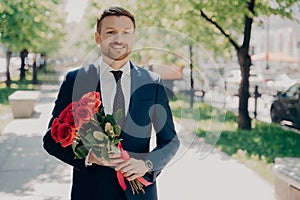 Smiling stylish stubbly gentleman in dark blue tuxedo with big bouquet photo