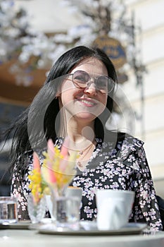 Smiling stylish woman in black shirt with sunglasses sitting at the table drinking coffee in the terrace of restaurant