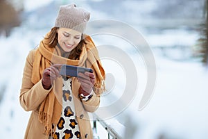 smiling stylish woman in brown hat and scarf using phone app