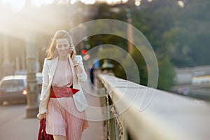 smiling stylish woman in dress and jacket in city using phone