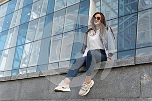 Smiling stylish woman on city street. Young woman in sunglesses in youth clothing on the city street