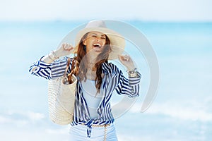 smiling stylish woman on seashore with straw bag