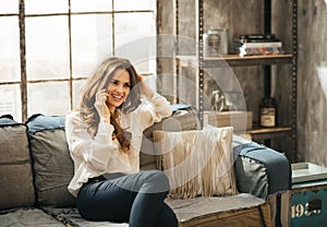 Smiling stylish woman sitting on divan and talking smartphone