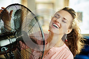 Smiling stylish woman using metallic floor standing fan
